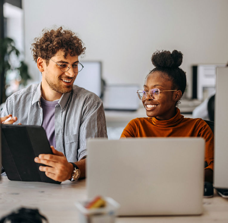 To kolleger på et kontor som samarbeider om arbeidsstyring, vaktplan og tidsregistrering ved bruk av digitale verktøy