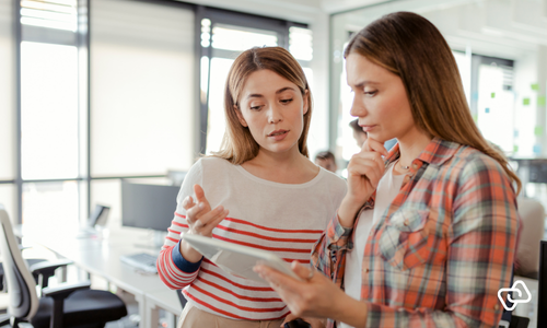 Kvinnelig leder i en liten bedrift gjennomgår digital timeregistrering på nettbrett sammen med ansatt – effektiv workforce management, timeregistrering og vaktplan for små virksomheter med fokus på lønn og kostnadskontroll.