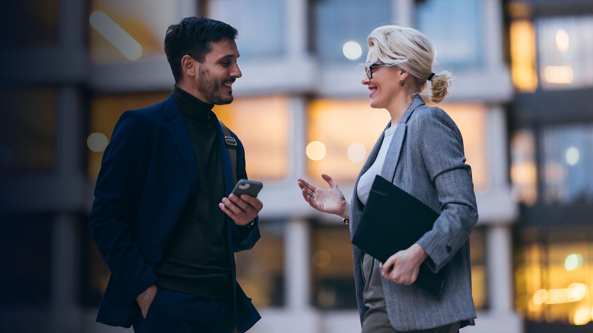 To kolleger i en forretningssetting som diskuterer arbeidsstyrkeplanlegging og effektiv medarbeiderhåndtering med bruk av en mobil enhet.