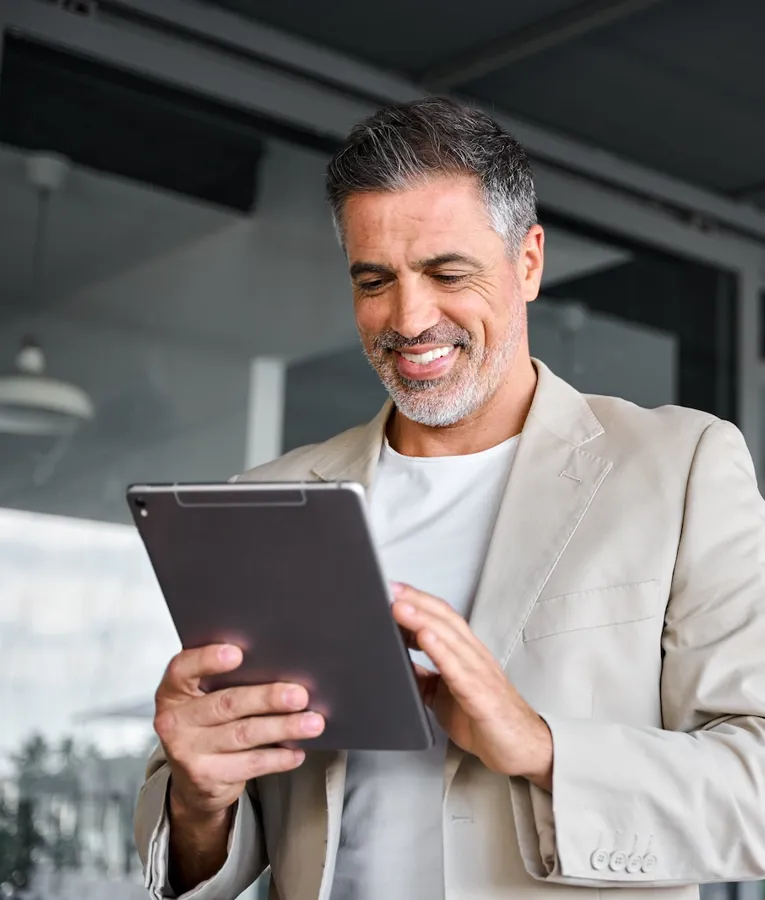 Smilende profesjonell mann i beige blazer bruker nettbrett utendørs – representerer mobil arbeidsstyrke, digitale verktøy og fleksible arbeidssituasjoner.