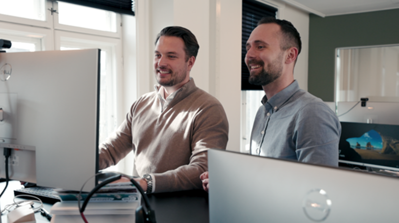 To kollegaer samarbeider foran dataskjerm om digital vaktplanlegging og timeregistrering i et moderne workforce management-system.