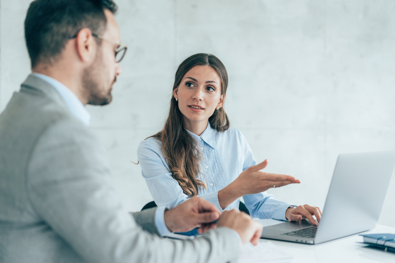 To kolleger som diskuterer AI-basert Workforce Management foran en bærbar PC, med fokus på smartere vaktplanlegging og timeregistrering på arbeidsplassen.