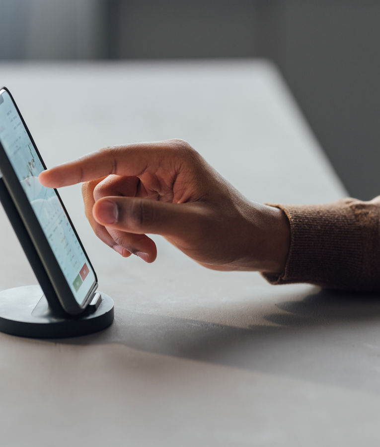 Nærbilde av en person som bruker en smarttelefon på en holder, og interagerer med en finans- eller dataanalyseapp som viser diagrammer og grafer. Ideell for innhold om mobil workforce management, produktivitetsapper eller digitale forretningsverktøy.