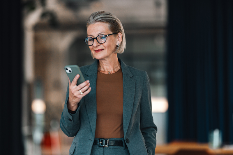 Leder som sjekker vaktplaner og timeregistrering på en smarttelefon gjennom en AI-drevet Workforce Management-løsning, med oversikt over ansatte og planlegging.