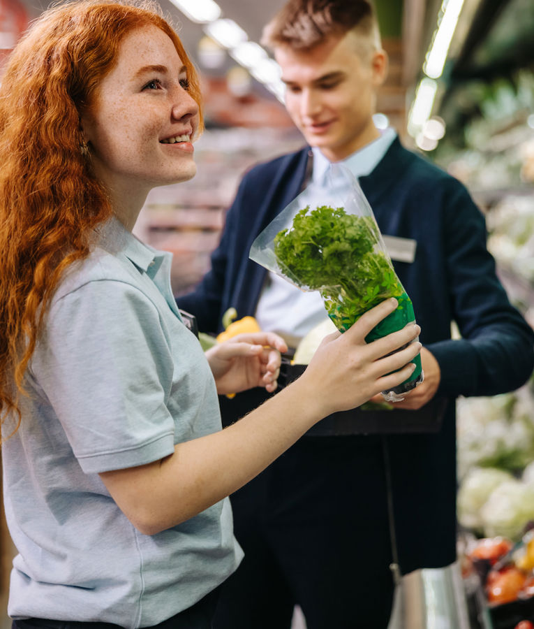 En vennlig butikkansatt hjelper en kunde med å velge ferske økologiske produkter og skaper en god handleopplevelse.