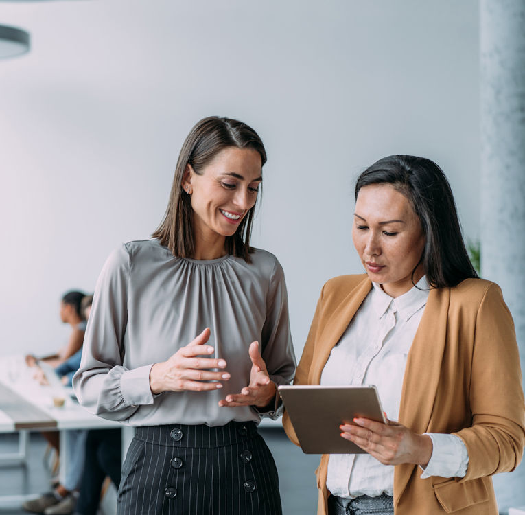 To profesjonelle kvinner samarbeider med et nettbrett i et moderne kontorlandskap.