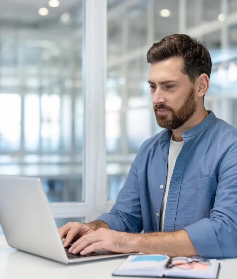 Kontoransatt jobber på laptop i moderne arbeidsmiljø, med digitale verktøy for vaktplanlegging, tidsregistrering og HR-administrasjon.