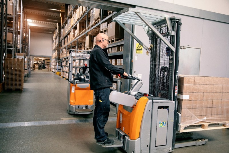 Lagerarbeider kjører palletruck i et moderne lager, der effektiv timeregistrering og vaktplanlegging sikrer optimal drift og bemanning.