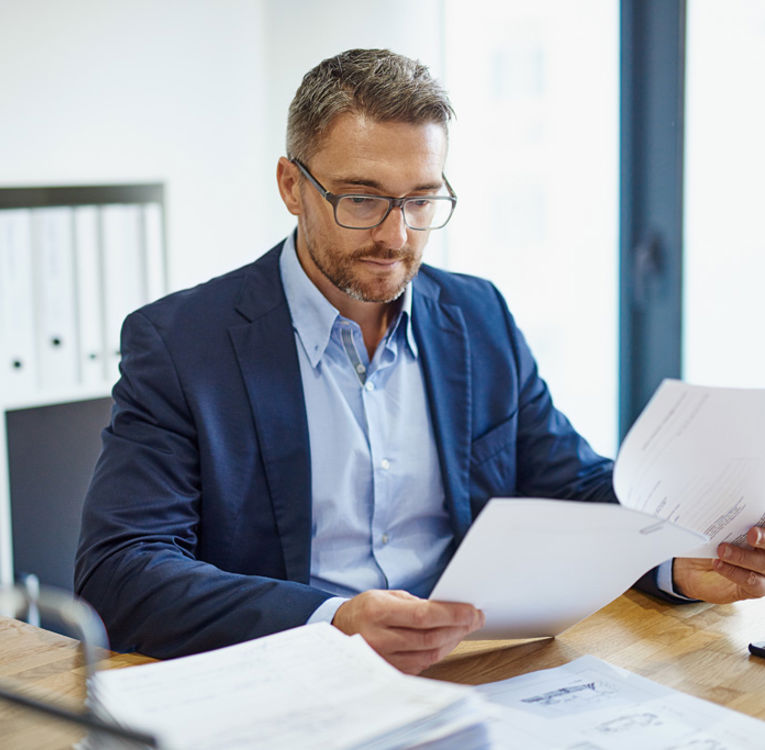 Mann i dress som gjennomgår dokumenter ved et skrivebord, som symboliserer profesjonalitet og strategisk arbeidsstyring og vaktplan