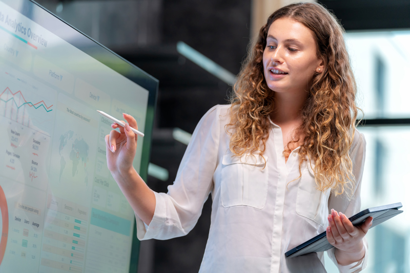 Kvinne som presenterer data og AI-analyser på en stor skjerm som en del av en presentasjon om Workforce Management, effektiv vaktplanlegging og timeregistrering i virksomheten.